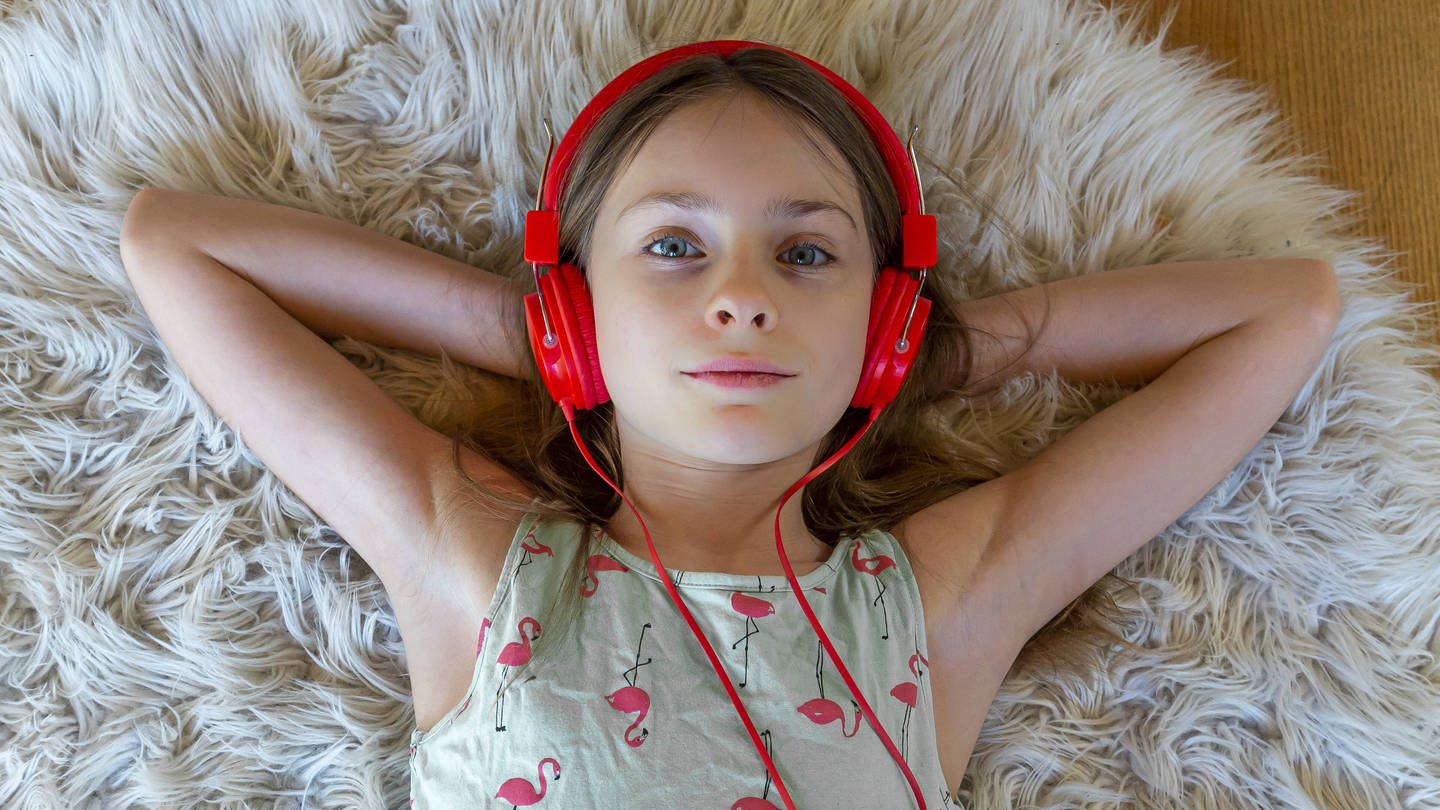 Ein Mädchen mit rotem Kopfhörern liegt auf dem Fußboden (Foto: IMAGO, Westend61)
