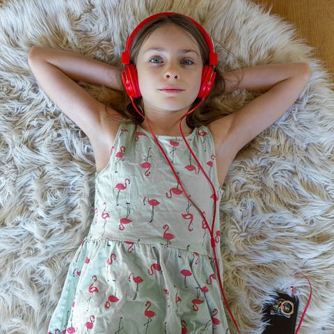 Ein Mädchen mit rotem Kopfhörern liegt auf dem Fußboden (Foto: IMAGO, Westend61)