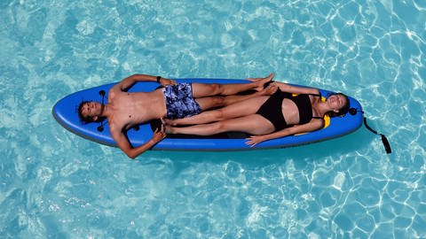 Junges Paar liegt in einem Swimmingpool auf einem SUP-Board (Foto: IMAGO, Frank Sorge)