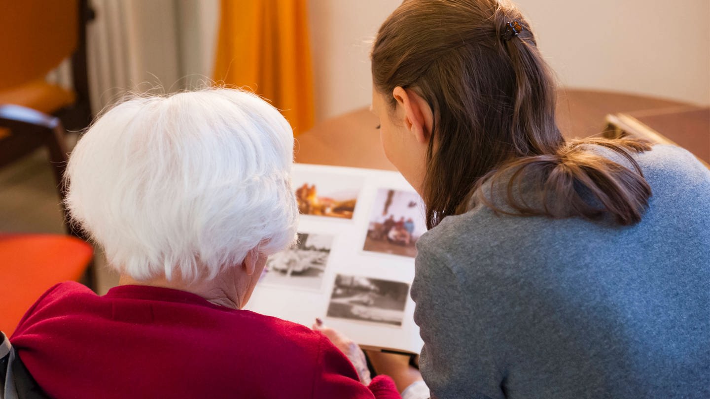 Enkelin schaut mit ihrer Großmutter ein Fotoalbum an (Foto: IMAGO, Westend61)