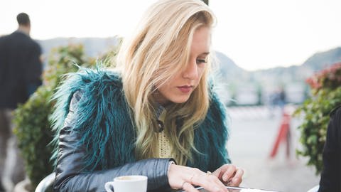 Junge Frau in Lederjacke, sitzt in einem Cafe und benutzt ein Tablet (Foto: IMAGO, Image Source)