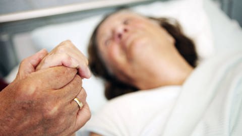 Hand einer alten Frau im Krankenbett wird gehalten (Foto: IMAGO, imago/imagebroker)