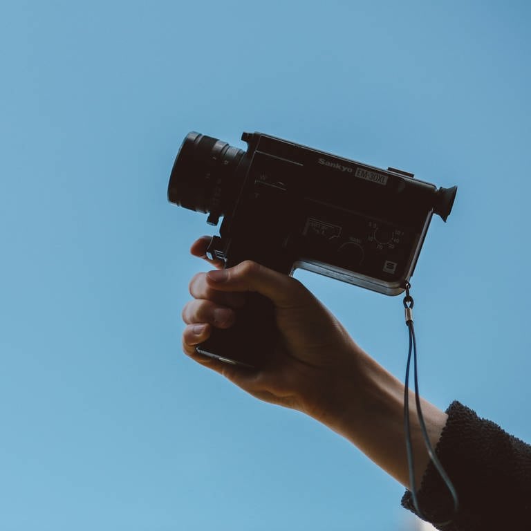 eine Hand hält eine alte Videokamera in den Himmel (Foto: unsplash/Thomas William)