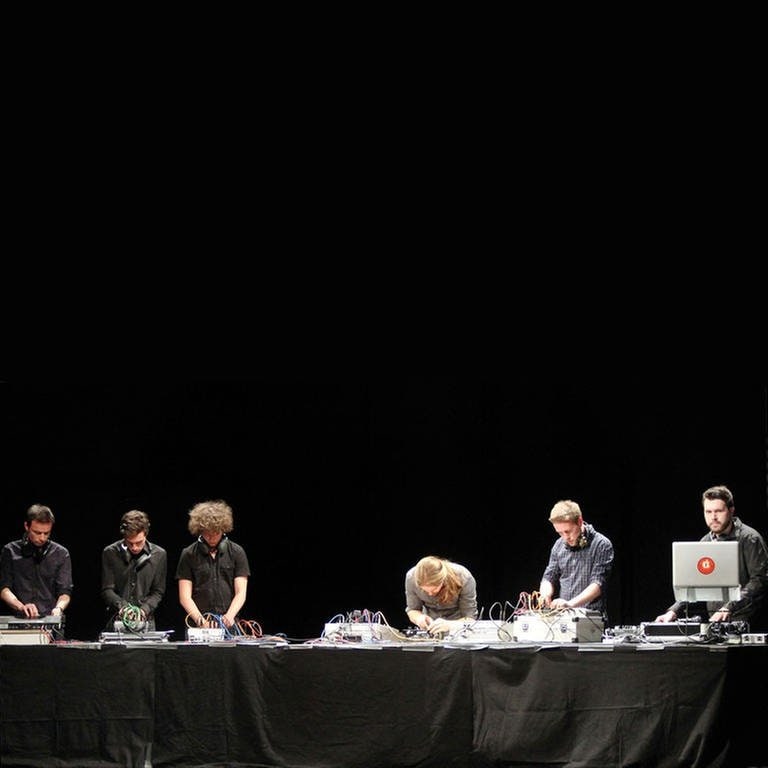sechs junge Männer stehen an einem langen Tisch und beugen sich über elektronische Geräte (Foto: SWR, SWR - Julia Vötig)