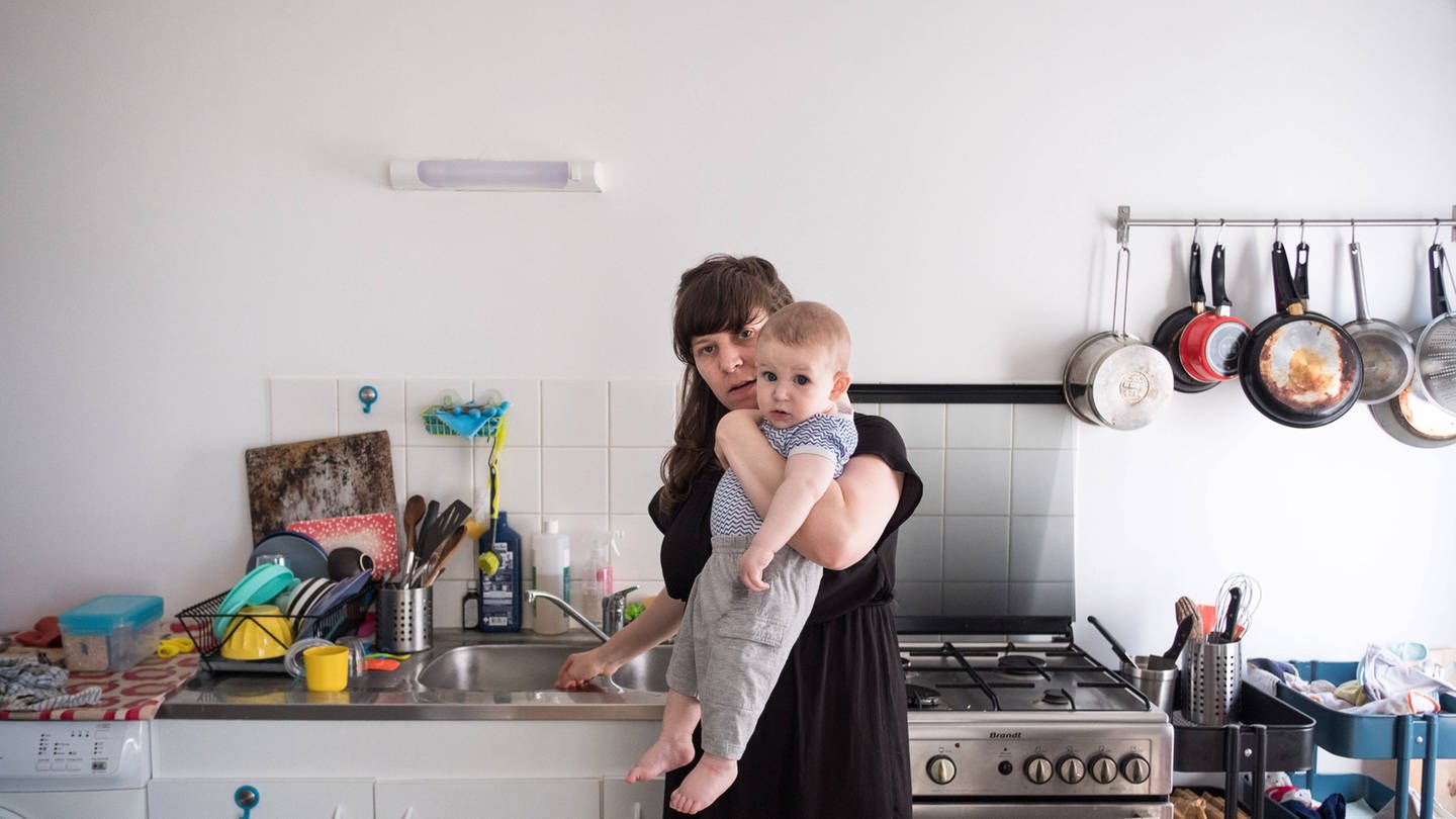 Mutter mit ihrem Kind auf dem Arm während der Hausarbeit (Foto: IMAGO, Hans Lucas)