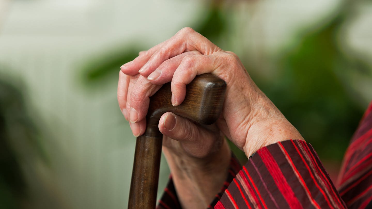 Hände einer alten Frau auf einem Gehstock