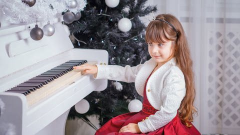 Mädchen vor Weihnachtsdekoration an einem weißen Klavier (Foto: imago images, IMAGO / agefotostock)
