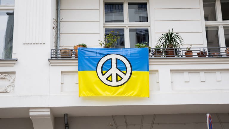 A Ukrainian flag with a peace sign hangs from a balcony in the Wilmersdorf district of Berlin in solidarity with Ukraine (Foto: dpa Bildfunk, Credit:Christoph Soeder / Avalon)