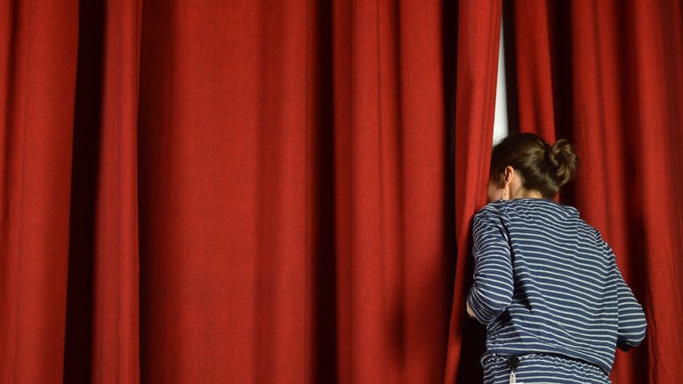 Eine Frau schaut durch einen Schlitz in einem roten Vorhang.  (Foto: IMAGO, IMAGO / Panthermedia)