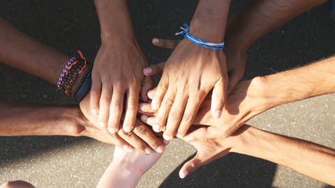 Hände berühren sich in der Mitte des Bildes, einige tragen bunte Armbänder, sie haben unterschiedliche Schattierungen der Hautfarbe. (Foto: IMAGO, IMAGO / agefotostock)