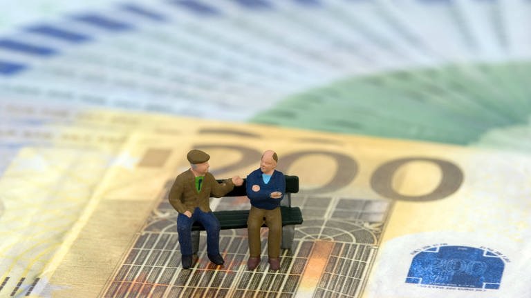 Zwei ältere Männer als Plastikfiguren sitzen auf einer Parkbank auf aufgefächerten Euroscheinen (Foto: IMAGO, IMAGO / blickwinkel)