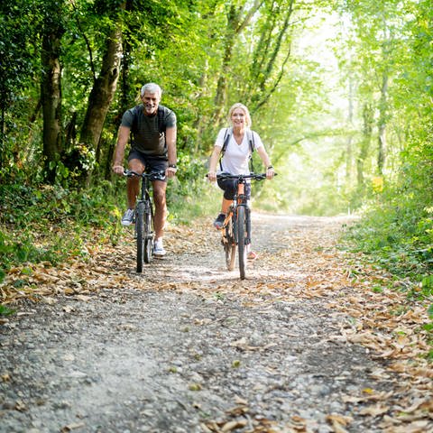 Paar fährt mit dem Fahrrad durch den Wald (Foto: IMAGO, PhotoAlto / Frédéric Cirou)