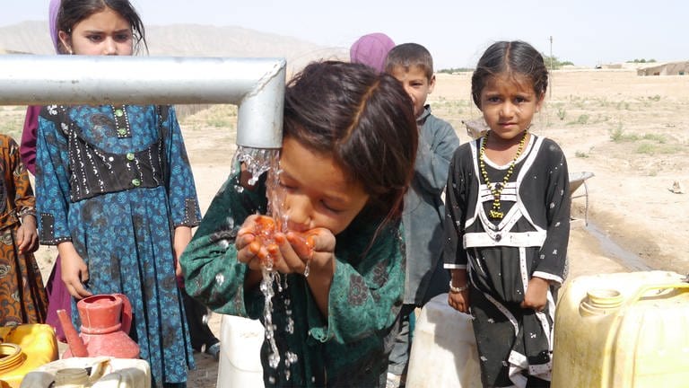 Bild von einem Kind beim Trinken an einem Brunnen. Andere Kinder stehen drum herum. Nur 30 Prozent der ländlichen Bevölkerung hat sicheres Trinkwasser. Das Brunnenbohren geht weiter.  (Foto: Afghanischer Frauenverein e.V.)