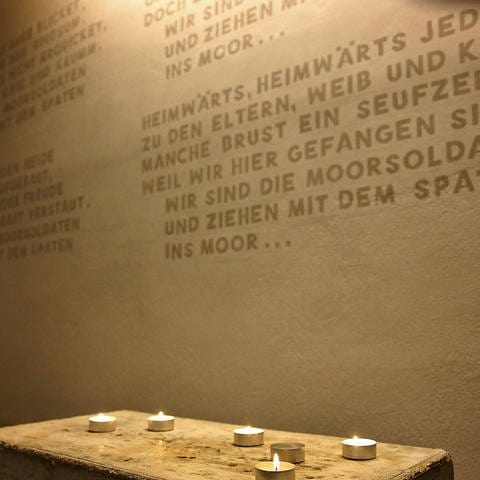Kerzen brennen im Gedenkraum vor dem in die Wand eingravierten Lied der Moorsoldaten (Foto: IMAGO, epd)