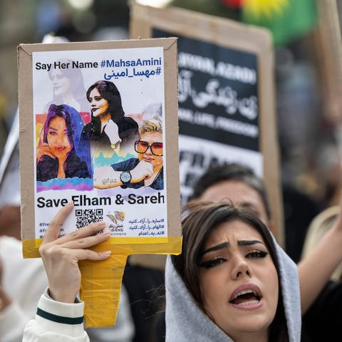 Demonstrantinnen und Demonstranten während einer Kundgebung gegen das politische Regime im Iran. Dabei steht auf einem Schild «Say her name #Mahsa Amini».  (Foto: dpa Bildfunk, picture alliance/dpa | Boris Roessler)