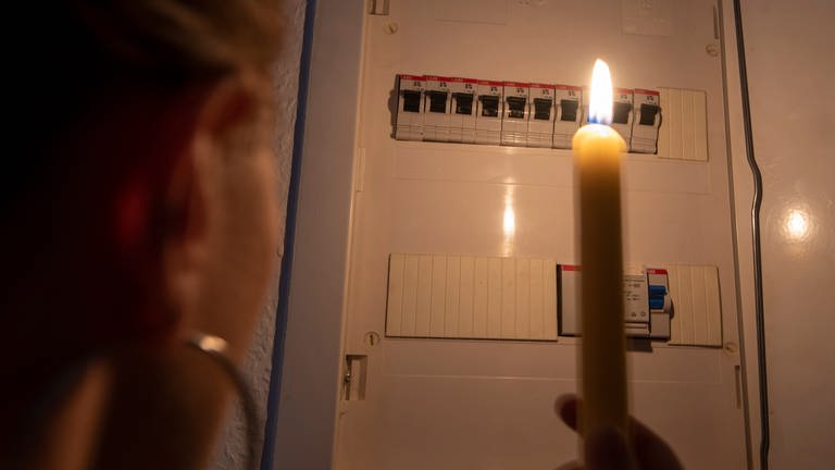 Eine Frau hält bei einem Stromausfall eine Kerze in der Hand und blickt in einen Sicherungskasten. (Foto: picture-alliance / Reportdienste, dpa-Zentralbild | Stephan Schulz)