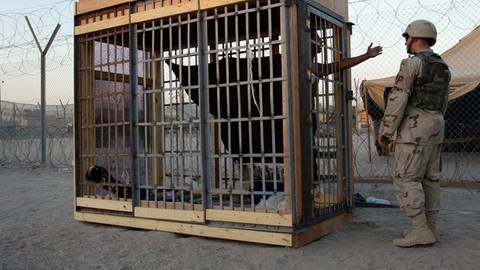 Ein Häftling in einer Einzelzelle im Freien spricht mit einem Militärpolizisten im Abu-Ghraib-Gefängnis am Stadtrand von Bagdad. (Foto: picture-alliance / Reportdienste, picture alliance / AP Photo | John Moore)