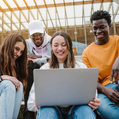 Eine Gruppe junger Leute schaut in einen Laptop (Foto: IMAGO, imago images/Addictive Stock)