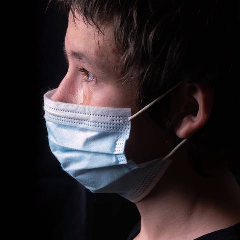 Weinender teenager mit medizinischer Gesichtsmaske vor schwarzem Hintergrund (Foto: IMAGO, IMAGO / CHROMORANGE)