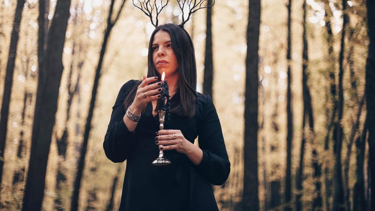 Eine Frau im dunklen Look mit brennender Kerze im Wald (Foto: picture-alliance / Reportdienste,  Zoonar | Dasha Petrenko)