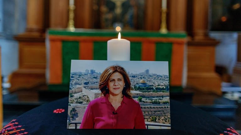 In Gedenken an die Journalistin Shireen Abu Akleh steht ein Foto von ihr vor einer Kerze (Foto: IMAGO, IMAGO / VXimages.com)