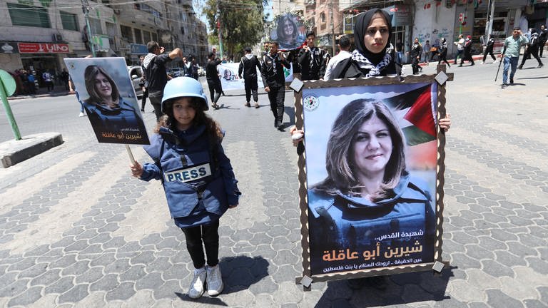 Nach dem Tod der palästinesischen Journalistin Shireen Abu Akleh trägt ein Mädchen eine kugelsichere Weste und Helm, in der Hand trägt sie ein Bild der getöteten Journalistin  (Foto: IMAGO, IMAGO/ZUMA Wire)