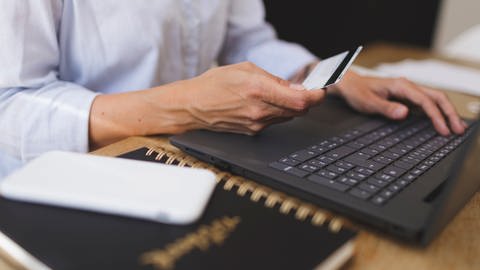 Digital Detox statt Onlineshopping? Ein Mann sitzt vor einem Laptop, in der Hand eine Bankkarte (Foto: IMAGO, imago images/imagebroker)