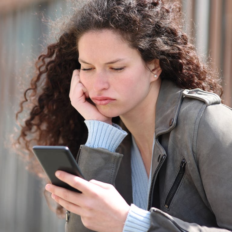 Bored woman checking smart phone in the street (Foto: IMAGO,  xPheelingsMediax Panthermedia31385627.jpg)