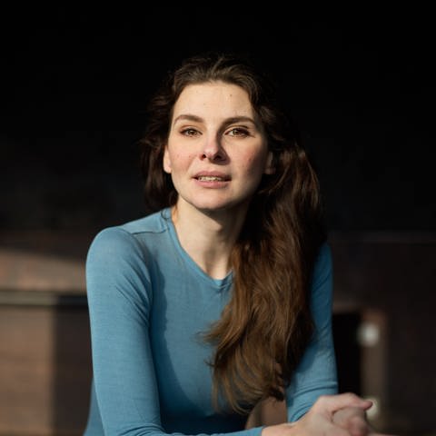 Judith Poznan mit offenen Haaren, in blauem Shirt vor dunklem Hintergrund (Foto: Pressestelle, Scarlett Werth)