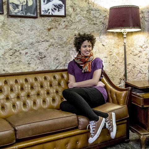 Die angolanische Sängerin Aline Frazao sitzt auf einem braunem Ledersofa (Foto: IMAGO, Foto: Jorge Amaral / Global Images)