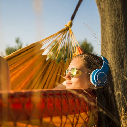 Frau mit Kopfhörern in einer Hängematte im Freien (Foto: imago images, IMAGO / Westend61)