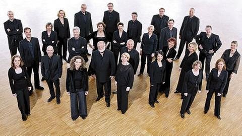 Die Sängerinnen und Sänger vom SWR Vokalensemble Stuttgart stehen, schwarz gekleidet, in einer lockeren Gruppe auf einem Parkettboden (Foto: SWR, SWR - Christian Mader)
