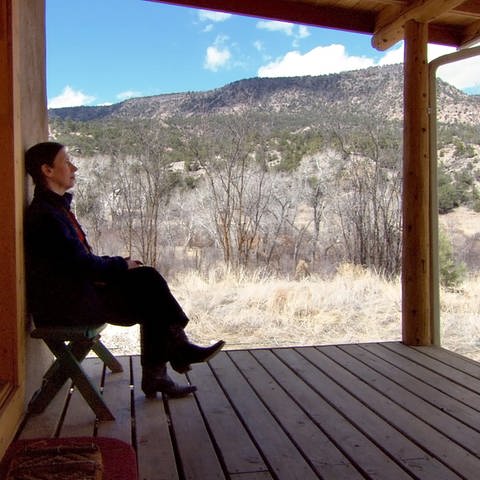 Auf dem Foto sieht man Meredith Monk von der Seite  sitzend auf der Terasse eines Hauses. Im Hintergrund sind Berge zu sehen.  (Foto: ECM Records / Foto: Babeth Van Loo)