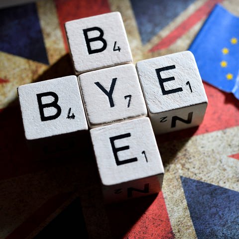 Würfelbuchstaben formen den Schriftzug Bye-bye auf der Fahne von Großbritannien neben einer zerrissenen EU-Fahne (Foto: IMAGO, IMAGO / Christian Ohde)