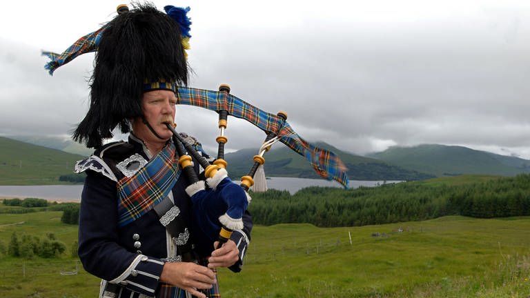 Ein Dudelsackspieler in den Farben des Clans MacBeth spielt im Hochland bei Glen Coe in Schottland für die Touristen, aufgenommen am 09.07.2005. (Foto: picture-alliance / Reportdienste, picture-alliance/ dpa/dpaweb | Tim Brakemeier)