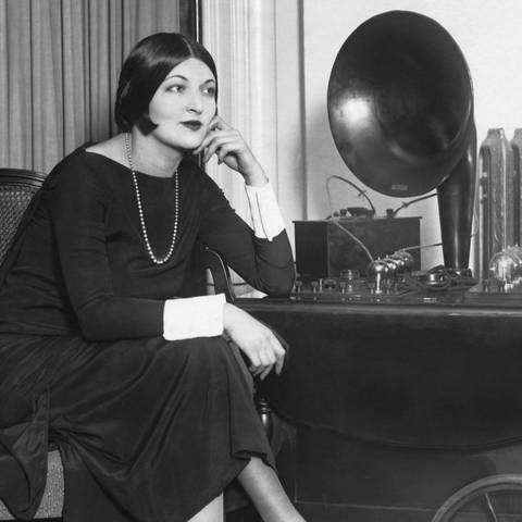 Schwarz-weiß: Frau mit Perlenkette und 1920er Frisur hört Radio (Foto: IMAGO, IMAGO / UIG)