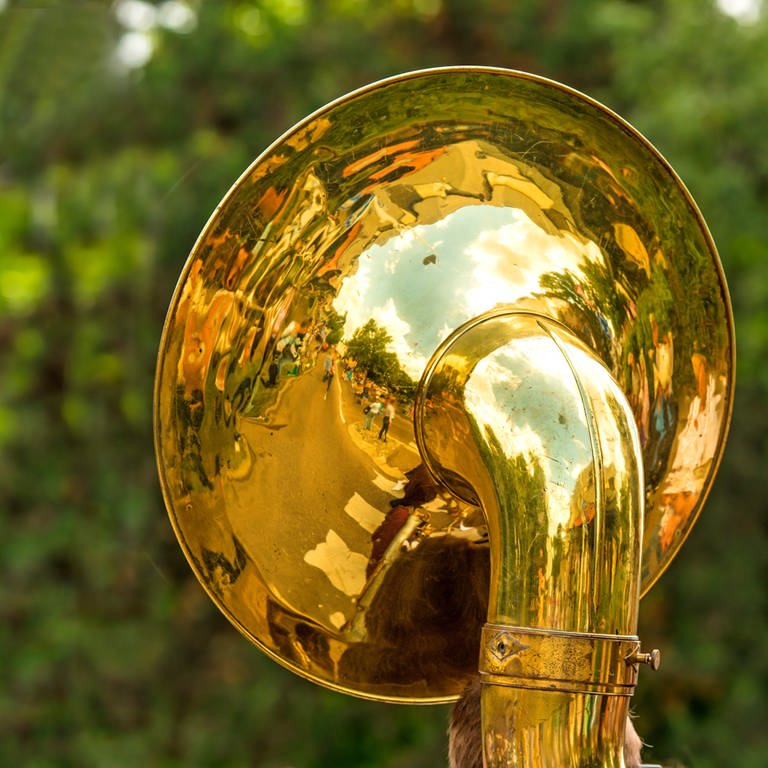 Der goldglänzende Trichter einer Tuba vor verschwommenem grünem Hintergrund (Foto: IMAGO, IMAGO / Panthermedia)