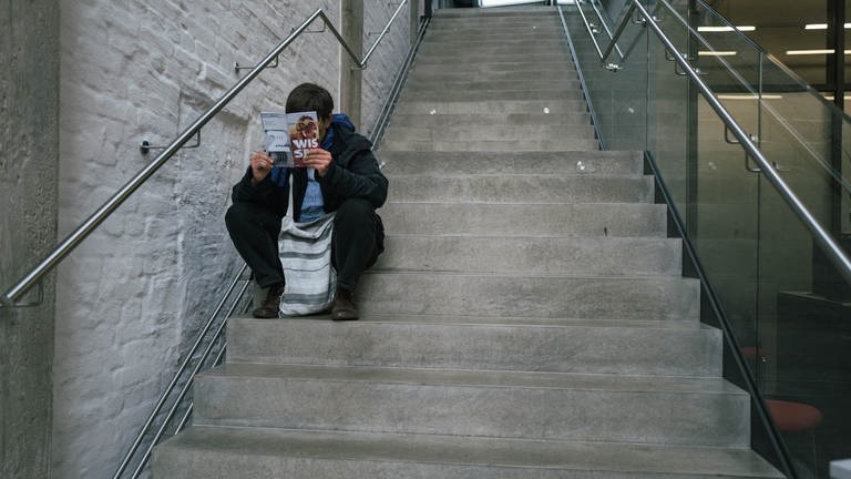 Mann sitz auf Treppe und liest in Broschüre (Foto: SWR, Oliver Matlok)