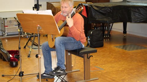Mann mit Gitarre sitzt hinter Notenpult und probt (Foto: SWR)