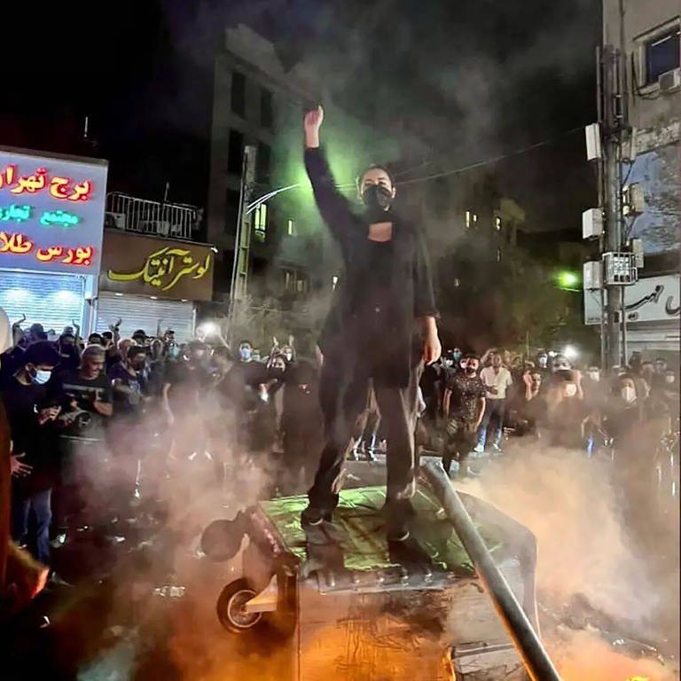 Eine Frau bei einer Demonstration im Iran, die auf einer großen Mülltonne steht und den Arm hebt (Foto: IMAGO, IMAGO / ZUMA Wire)