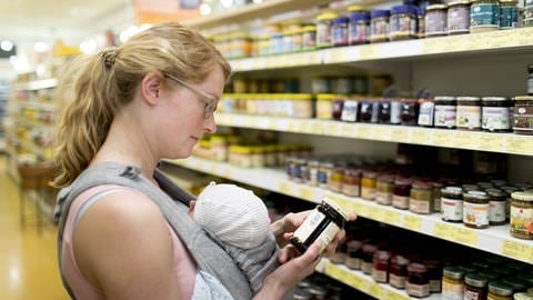 Mutter mit Säugling informiert sich beim Einkauf über die Inhaltsstoffe eine Produkts. Immer mehr Konsumenten wollen genau wissen, was in den Lebensmitteln steckt und erhöhen damit den Druck auf die Industrie. (Foto: IMAGO, imago images / photothek)