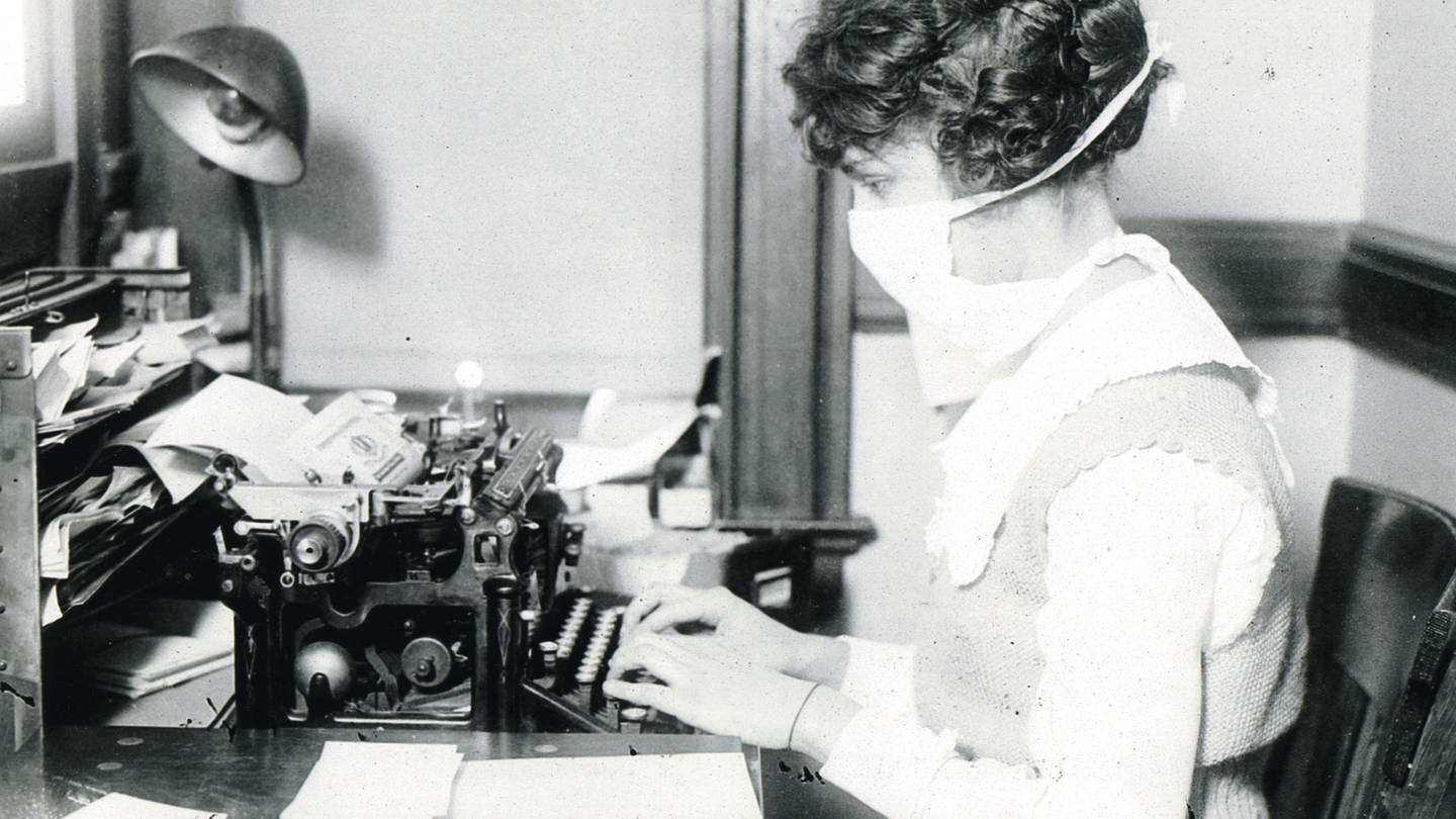 Schreibkraft mit Mund-Nasen-Schutz während der Spanischen Grippe um 1918