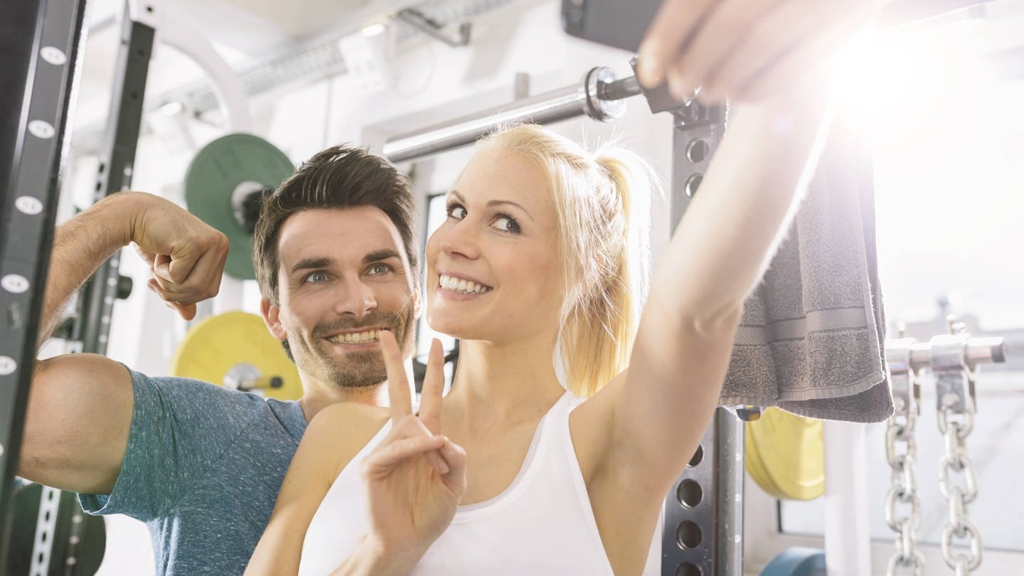 Junges Paar macht ein Selfie im Fitness-Studio: Teenager wetteifern um den perfekten Körper und posten Bilder in den sozialen Medien von möglichst dicken Muskeln oder möglichst dünnen Oberschenkeln