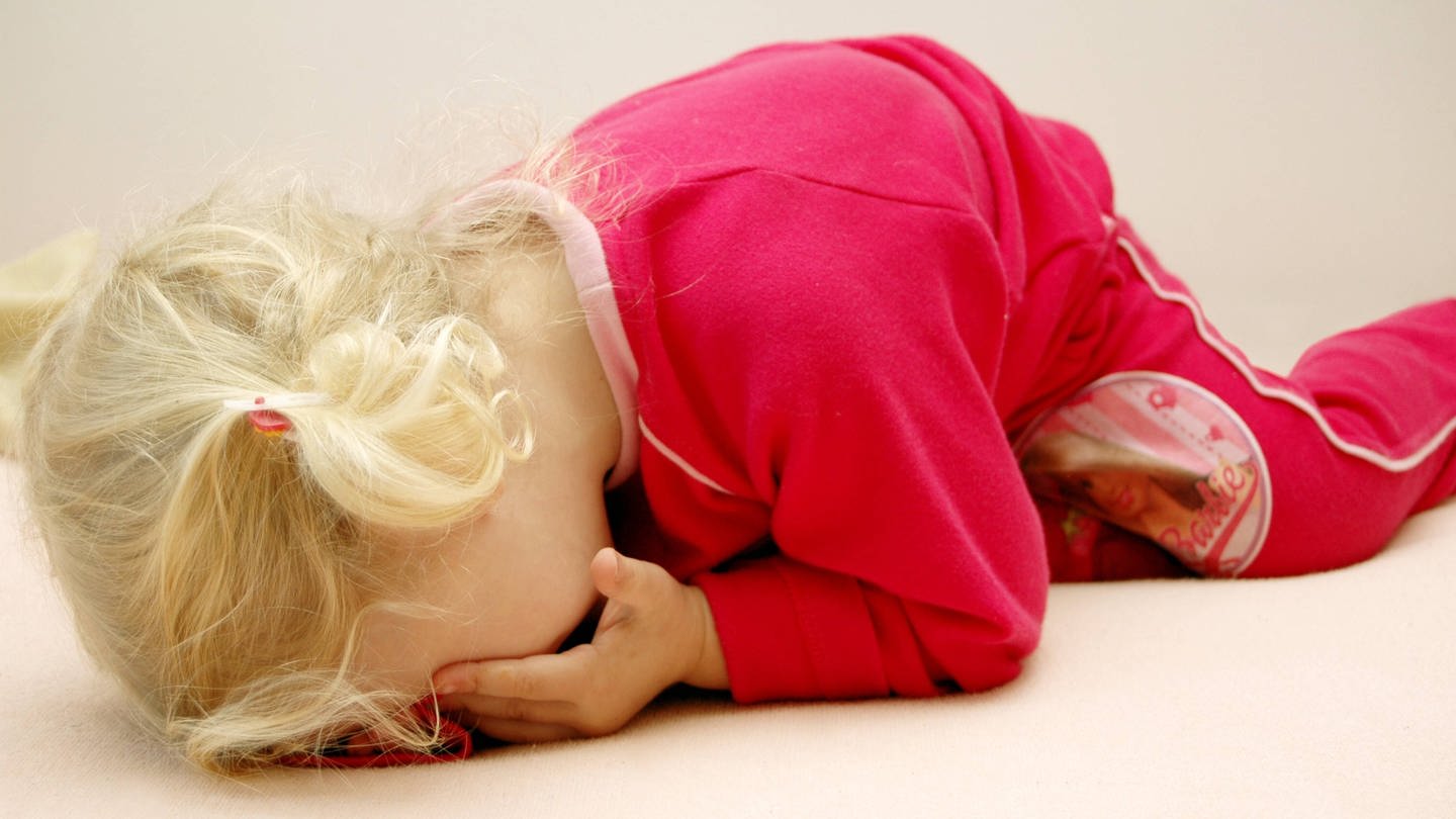 Kleines Mädchen liegt weinend auf dem Boden. Traumatische Erlebnisse können sich massiv auf Seele und Körper auswirken. Wissenschaftler erforschen unter anderem, wie sich traumatisierte Kinder entwickeln. (Foto: IMAGO, imago images / imagebroker/begsteiger)