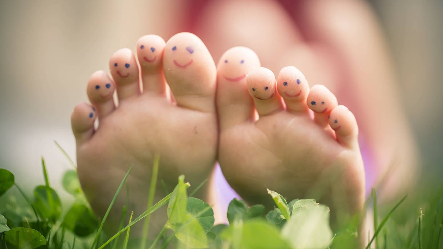 Füße im Gras mit auf die Zehen gemalten Gesichtern (Foto: IMAGO, imago images / Westend61)