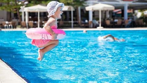 Ein kleines Mädchen mit Schwimmring hüpft in das Becken in einem Schwimmbad. (Foto: Getty Images, Thinkstock -)