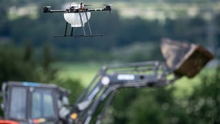 Eine Drohne fliegt vor einem Traktor über einem Getreidefeld. Mit "Smart Farming" sollen mit neuester Technik in der Landwirtschaft die Erträge gesteigert und die Nachhaltigkeit verbessert werden. (Foto: picture-alliance / Reportdienste, picture alliance/Fabian Sommer/dpa)