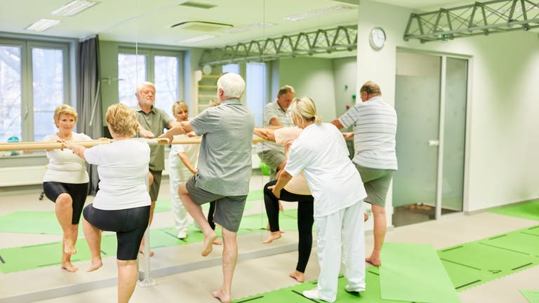 Therapeutin betreut Senioren bei Krankengymnastik an der Ballettstange als Sturzprophylaxe (Foto: picture-alliance / Reportdienste, picture alliance / Zoonar | Robert Kneschke)