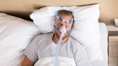 Mann mit Schlafapnoe und CPAP-Gerät: Menschen mit regelmäßigen Atemaussetzern sind häufig abgeschlagen und unkonzentriert (Foto: imago images, IMAGO / Panthermedia)