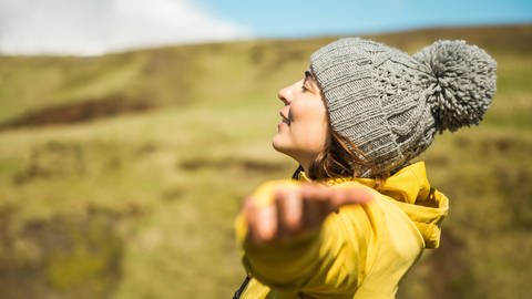 Junge Frau breitet in der Natur die Arme aus: Was ist Glück und wie können wir es finden? (Foto: IMAGO, IMAGO / Cavan Images)
